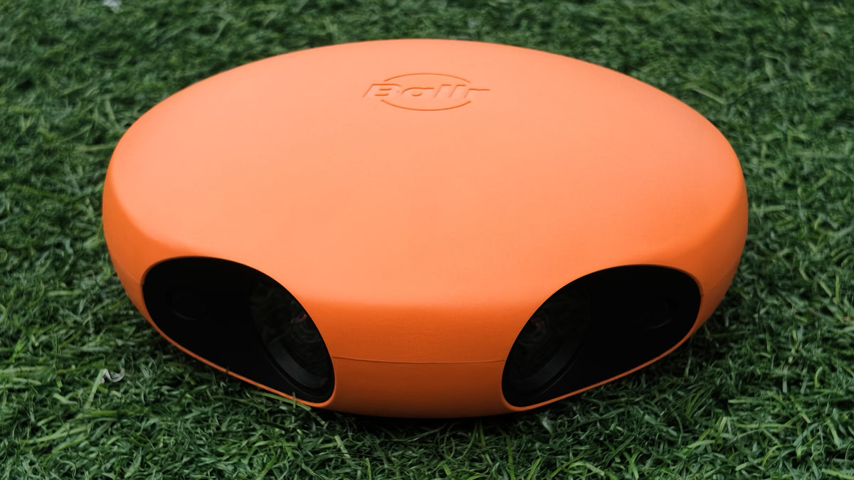 Close-up of the Ballr AI Sports Camera on grass showing the embossed Ballr logo and both wide-angle lenses