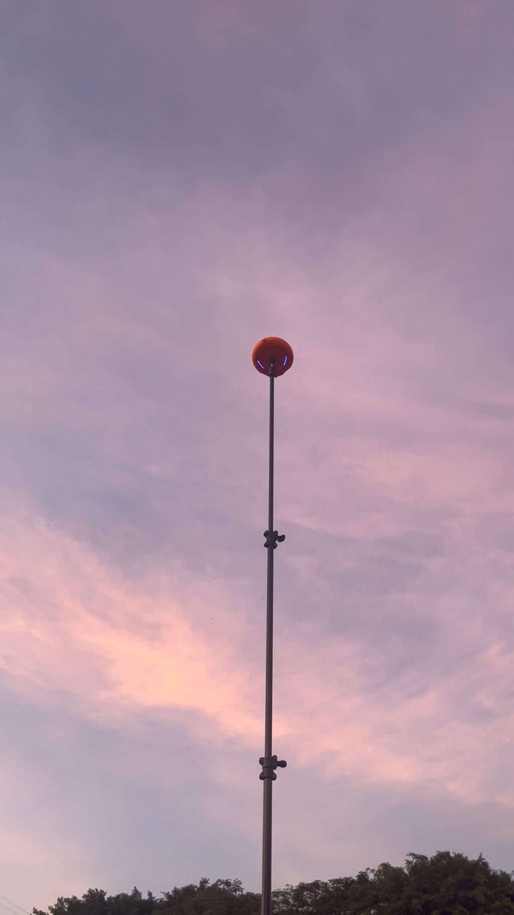 Ballr AI Sports Camera held level at the top of a raised pole against a sunset sky
